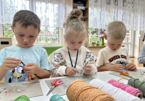 03 Dzieci przy stoliku nakładają szydełkami koraliki na sznurki