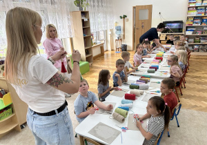 01 Pani pleciuga pokazuje dzieciom siedzącym przy stolikach gotowe breloczki