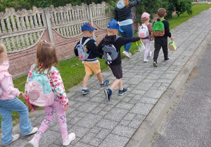 Zadowolone przedszkolaki z plecakami na plecach wracają do przedszkola