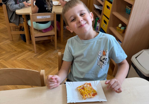Chłopiec z uśmiechem na twarzy zjada pizzę.