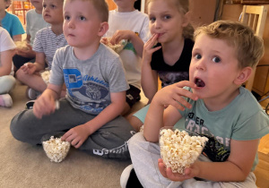 Dzieci zajadając popcorn oglądają bajkę.