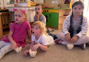 Dzieci zajadając popcorn oglądają bajkę.