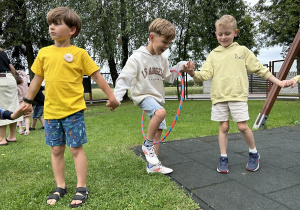 31 Chłopiec próbuje przejść przez hula hop, trzymając kolegów za ręce