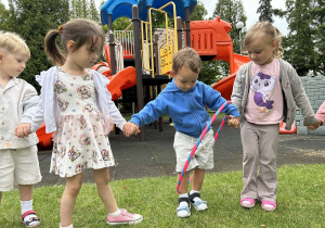 33 Chłopiec z grupy trzylatków przechodzi przez hula hop trzymając koleżanki za ręce