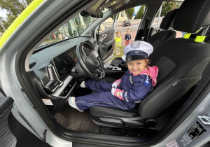Dziewczynka przebrana za policjantkę siedzi w radiowozie.