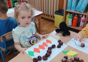 22. Dziewczynka układa kasztany i liście.