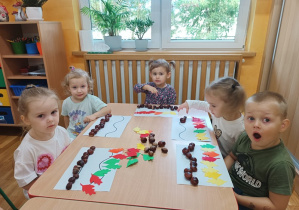 23. Dzieci układają wzór z kasztanów i liści.