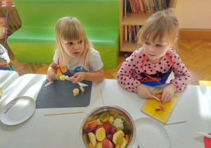 Dziewczynki kroją owoce plastikowymi nożami.