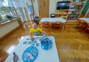 Chłopiec układa puzzle przy stoliku.