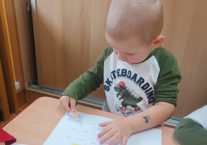 Chłopiec wkleja ilustrację Śmieszki do książeczki