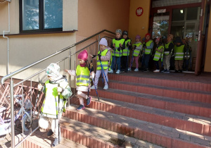 Dzieci ubrane w odblaskowe kamizelki z kijami w dłoni wychodzą z przedszkola.