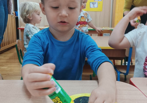 Chłopiec przykleja elementy do swojej pracy plastycznej