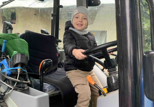 Chłopiec siedzi w traktorze.