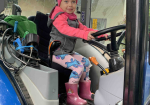 Dziewczynka trzyma kierownicę w traktorze.