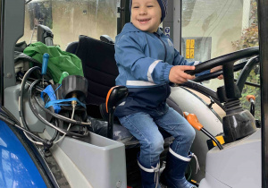 Uśmiechnięty chłopiec siedzi w traktorze.