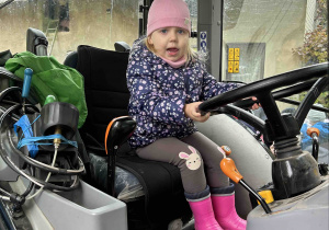 Dziewczynka trzyma kierownicę w traktorze.