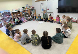 Dzieci siedzą w kole na dywanie.