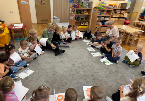 Dzieci siedzą w kole na dywanie z panią psycholog.
