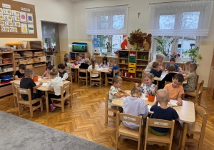 Dzieci siedzą przy stoliczkach.