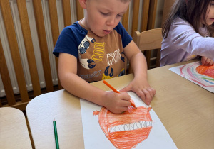 Chłopczyk starannie koloruje swój rysunek.