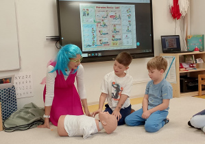 Chłopcy pod okiem Pani ratownik udzielają pomocy poszkodowanemu.