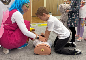 Pani tłumaczy chłopcy jak zrobić prawidłowe uciski.