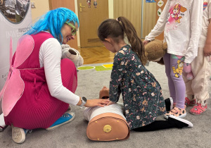 Dziewczynka pod okiem pani ratownik uczy się prawidłowych ucisków.