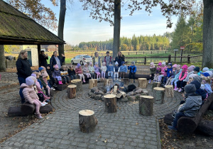 Przedszkolaki siedzą przy ognisku.
