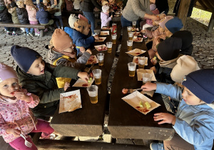 Maluszki jedzą kiełbaskę i piją herbatę.