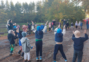 Dzieci z uniesionymi rękoma śpiewają piosenkę.