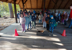 Przedszkolaki patrzą na dzieci biegnące z ziemniakiem na taczce.