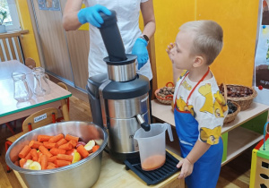 Chłopiec wrzuca warzywa do sokowirówki