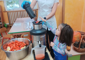 Dziewczynka wrzuca marchewkę do sokowirówki