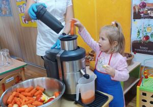 Dziewczynka wrzuca warzywa do sokowirówki