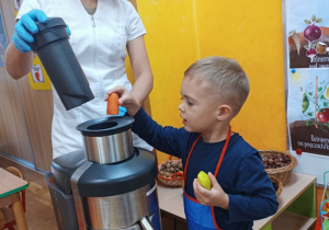 Chłopiec wrzuca jabłko do sokowirówki