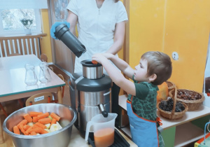 Chłopiec wrzuca marchewkę do sokowirówki