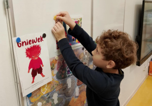 Chłopiec przyczepia ilustrację na tablicy.