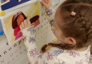 Dziewczynka przyczepia ilustracje na tablicy.