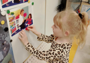 Dziewczynka przyczepia ilustracje na tablicy.