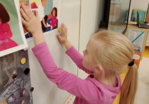 Dziewczynka przyczepia ilustracje na tablicy.