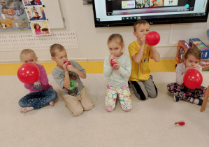 Dzieci dmuchają czerwone balony.