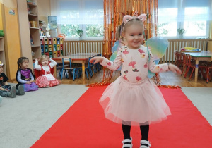 10. Dziewczynka w stroju motylka idzie po czerwonym dywanie.