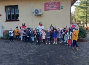 Dzieci z kijkami i biało-czerwonymi flagami stoją na tle budynku przedszkola