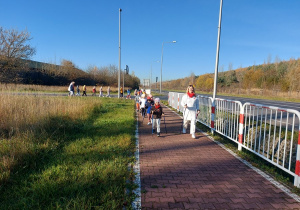 Zadowolone przedszkolaki z koltylionami na piersi idą z kijakmi