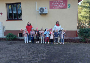 Dziewczynki z paniami stoją na tle budynku przedszkola