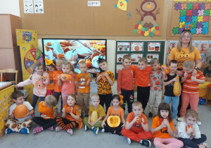 Dzieci ubrane w pomarańczowe koszulki, trzymają dynie w ręce i pozują do zdjęcia