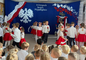 Dzieci idą w tańcu z białymi chustkami i różami.