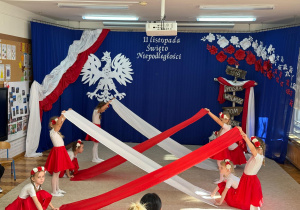 Dziewczynki tańczą z biało czerwonymi materiałami.