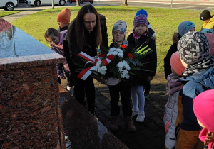 Dzieci składają kwiaty pod pomnikiem.