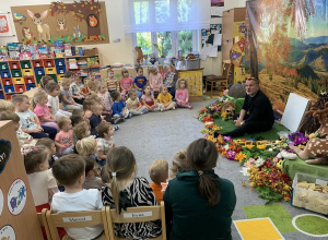 Dzieci siedzą na dywanie i słuchają prowadzącego warsztaty.